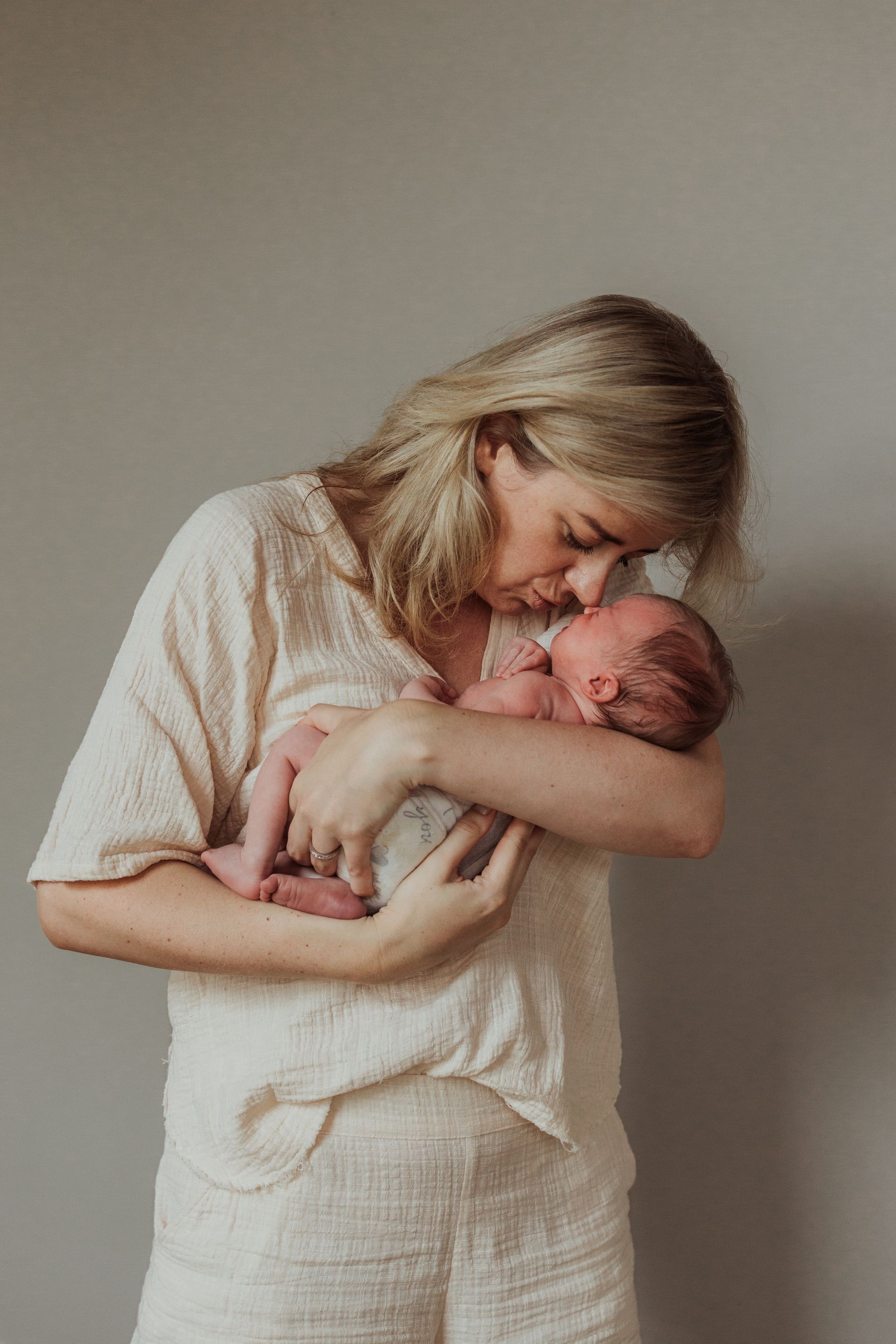 Een vrouw houdt een pasgeboren baby in haar armen en kust hem op de wang.
