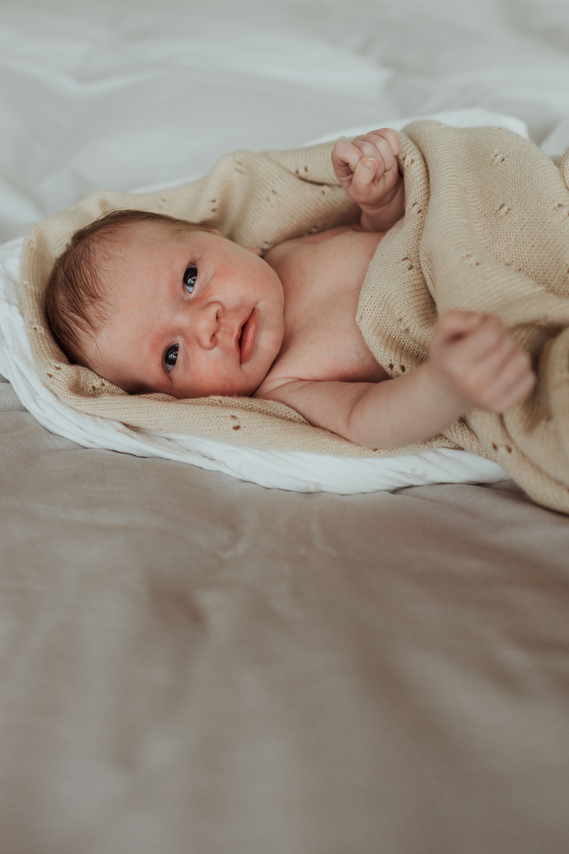 Een pasgeboren baby ligt op een bed, gewikkeld in een deken.