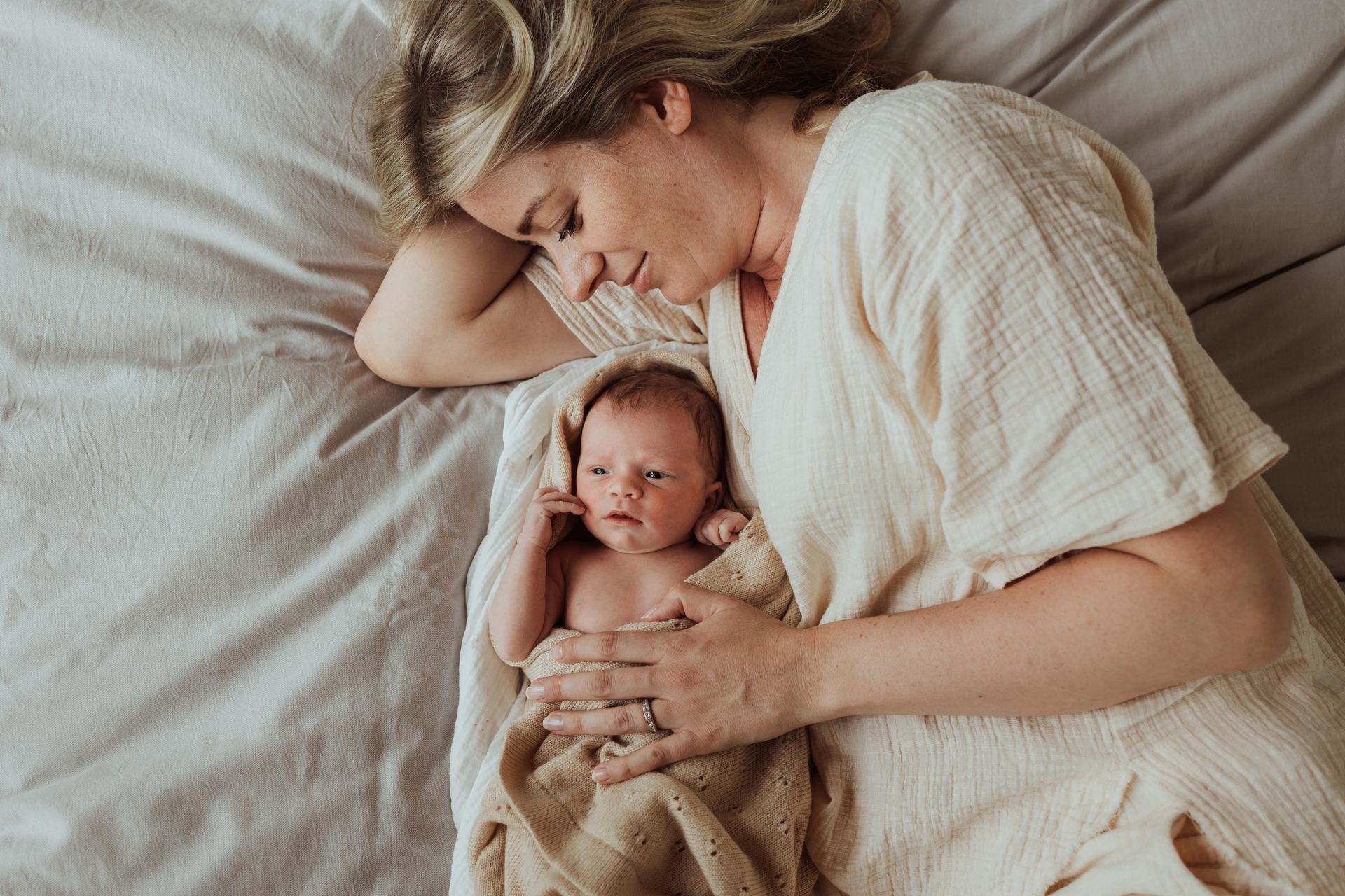 Een vrouw ligt op een bed met een pasgeboren baby in haar armen.