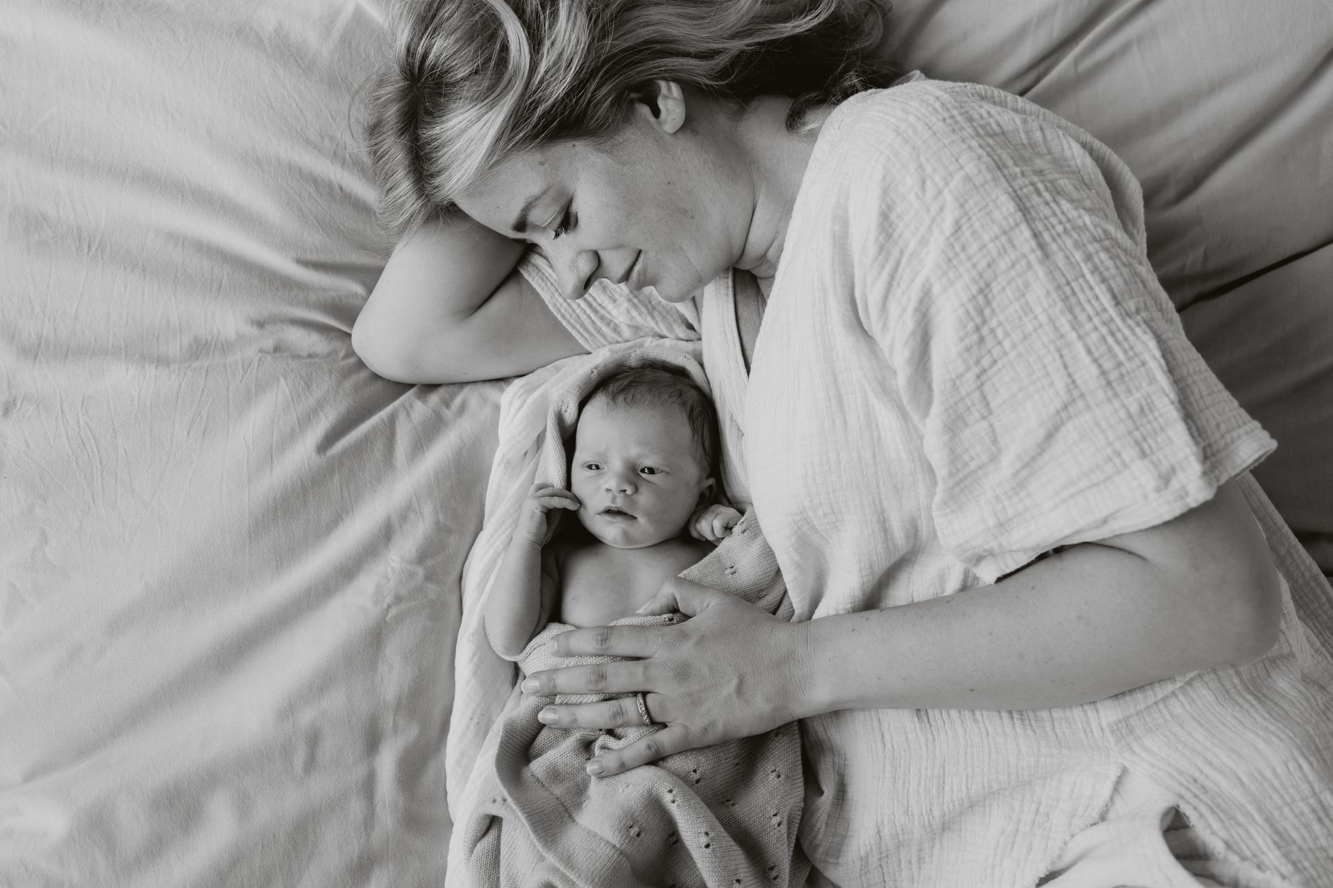 Een vrouw ligt op een bed met een pasgeboren baby in haar armen.