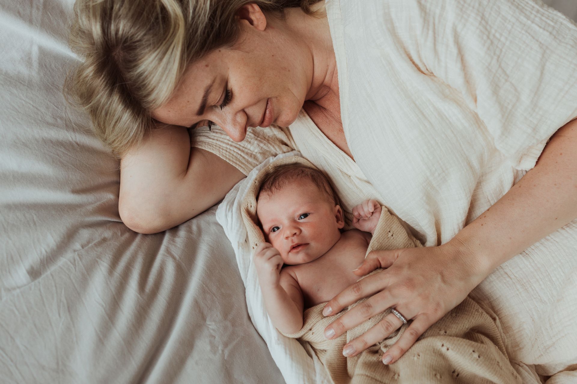 Een vrouw ligt op een bed met een pasgeboren baby, gewikkeld in een deken.