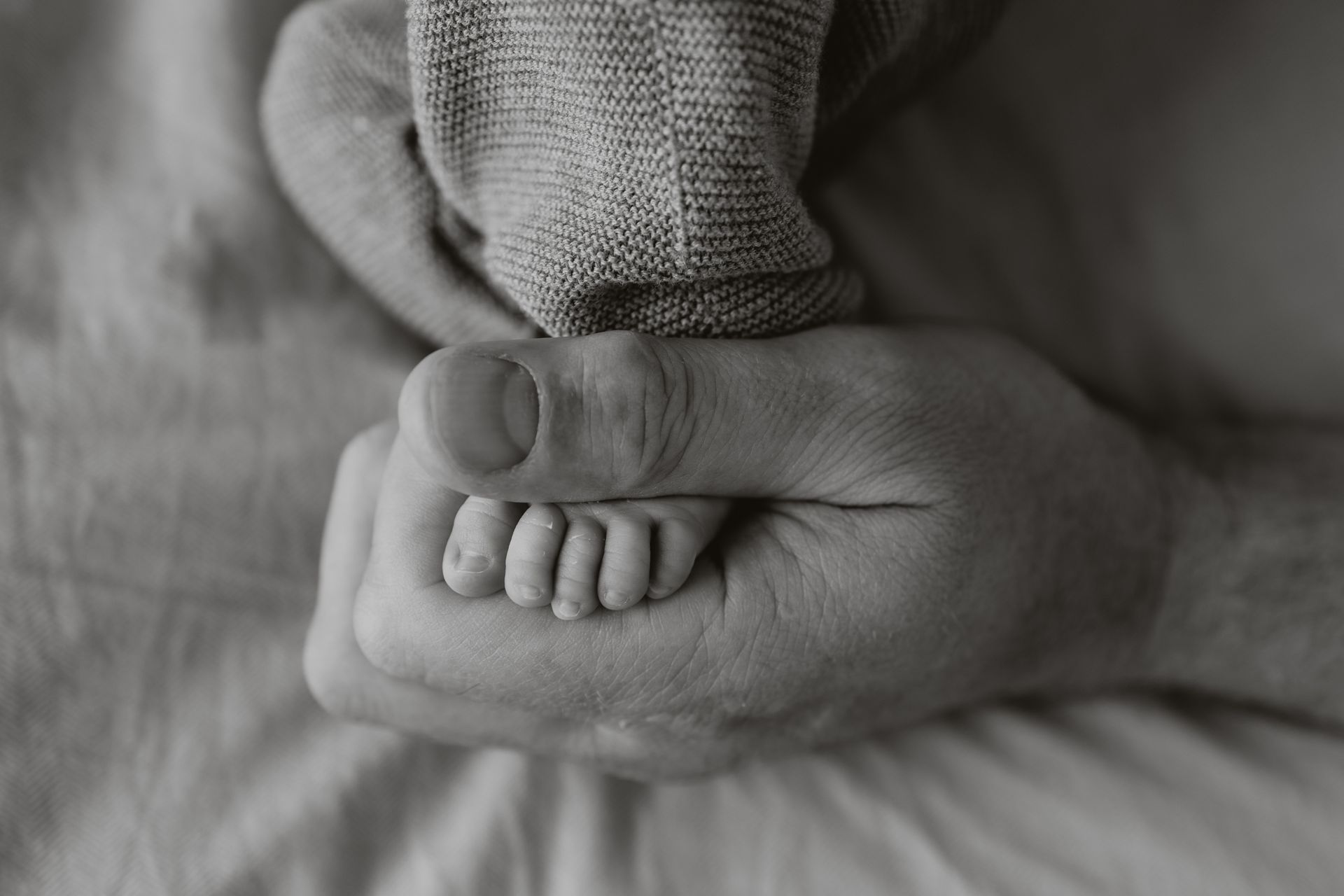 Een zwart-witfoto van pasgeboren babyvoetje in papa's hand.