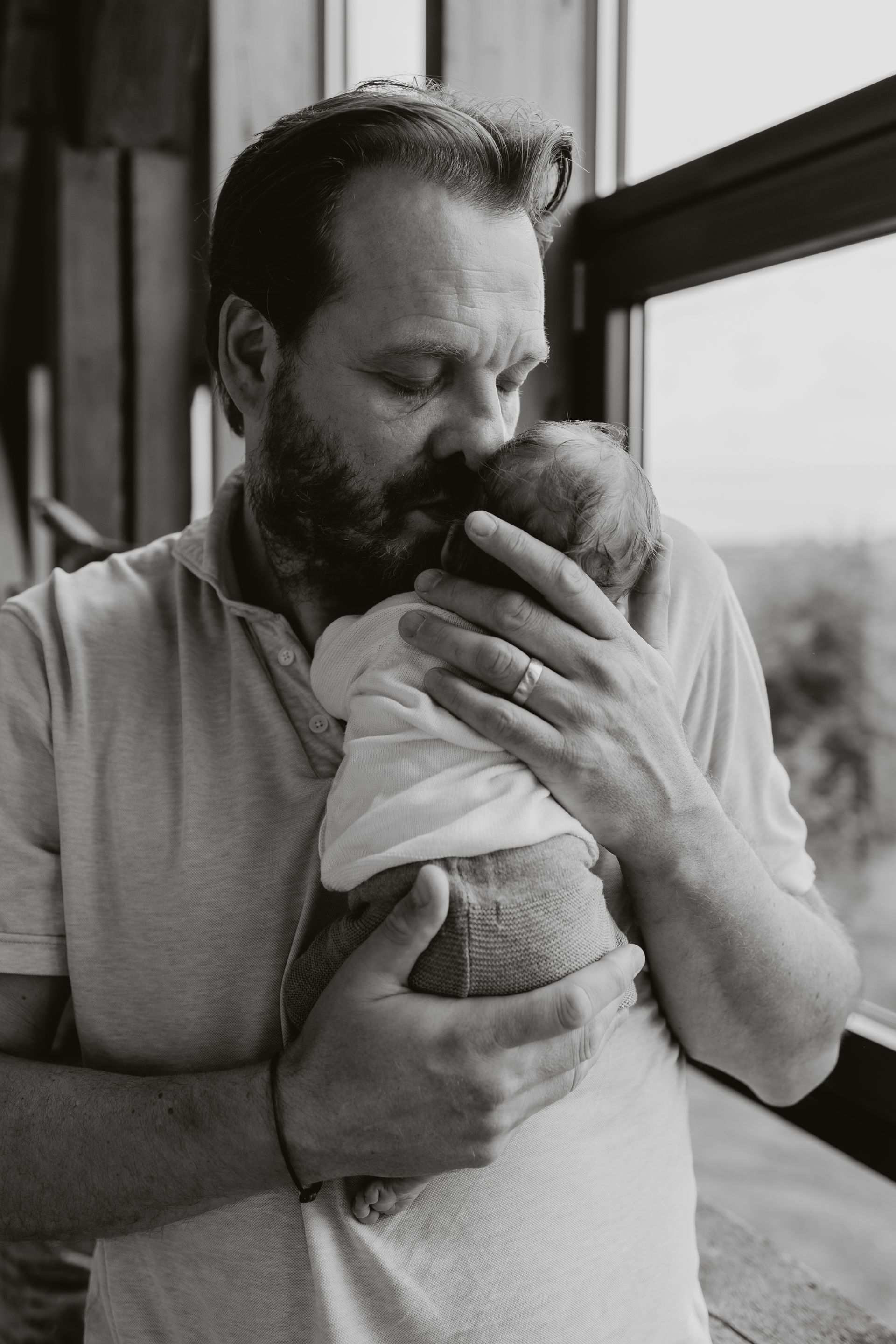 Een vader houd zijn pasgeboren baby in zijn armen en kust hem op de wang.