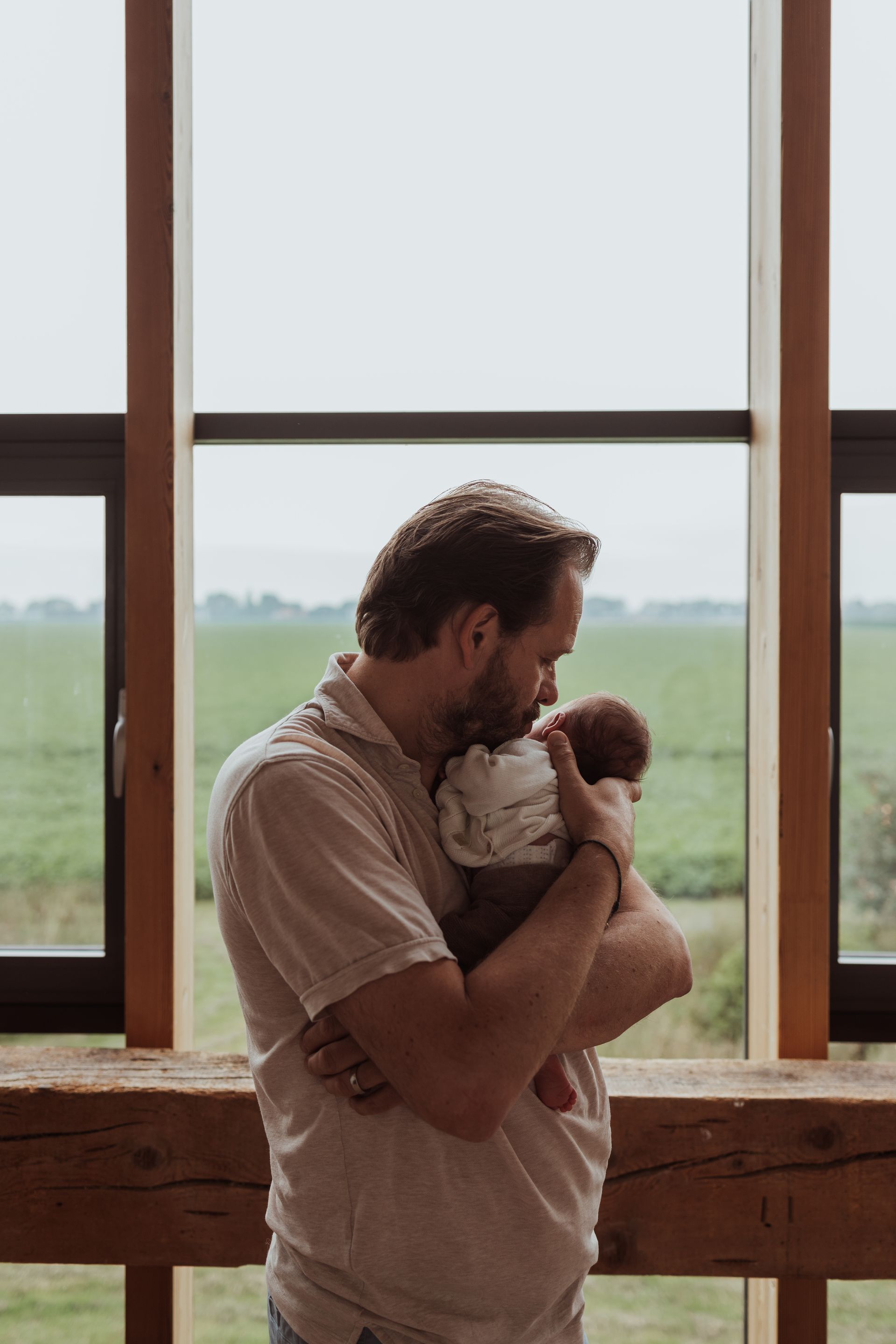 Een vader houdt zijn baby in zijn armen voor een raam.