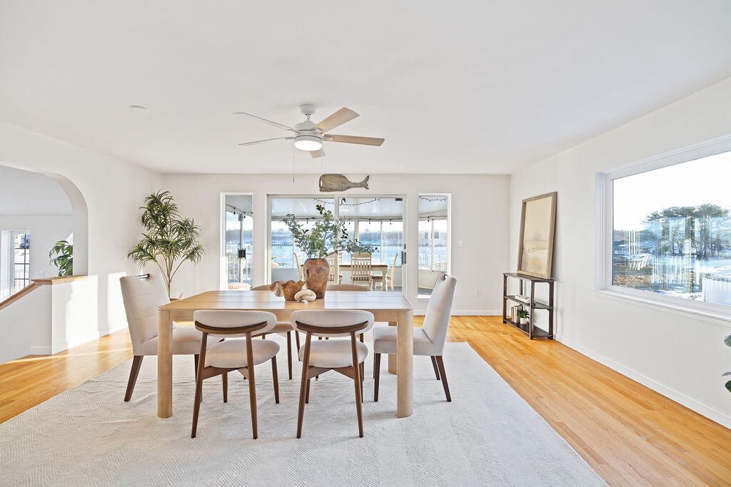Bright dining room with wooden table, white chairs, large windows, and ceiling fan