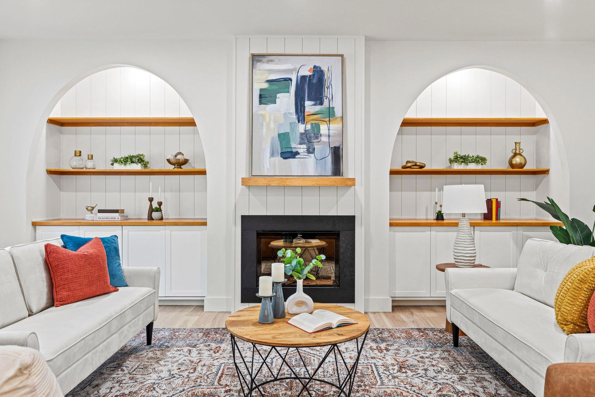 Bright living room with white sofas, built-in shelves, colorful pillows, and abstract wall art