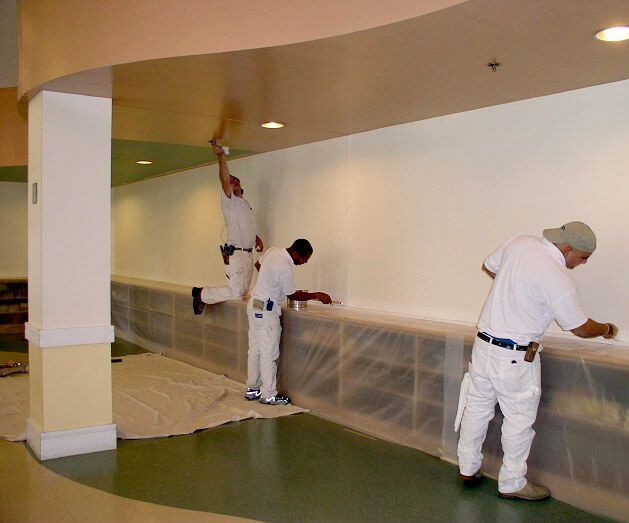 A group of men are painting a wall in a room