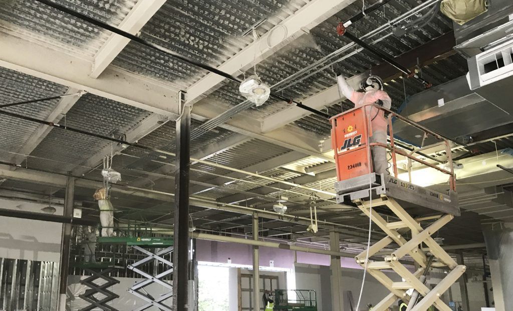 A man is standing on a scissor lift working on the ceiling of a building.