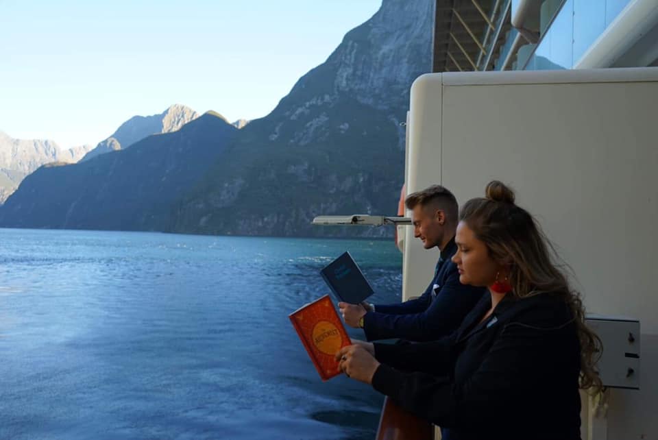 Xander Clemens is with Emily Beam on the Celebrity Solstice reading the books Great Thinkers and the alchemist by Paulo Coelho