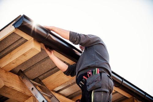 A Man Is Installing A Gutter On The Roof Of A Building - Southgate, MI - Cassino Construction & Cement Corporation