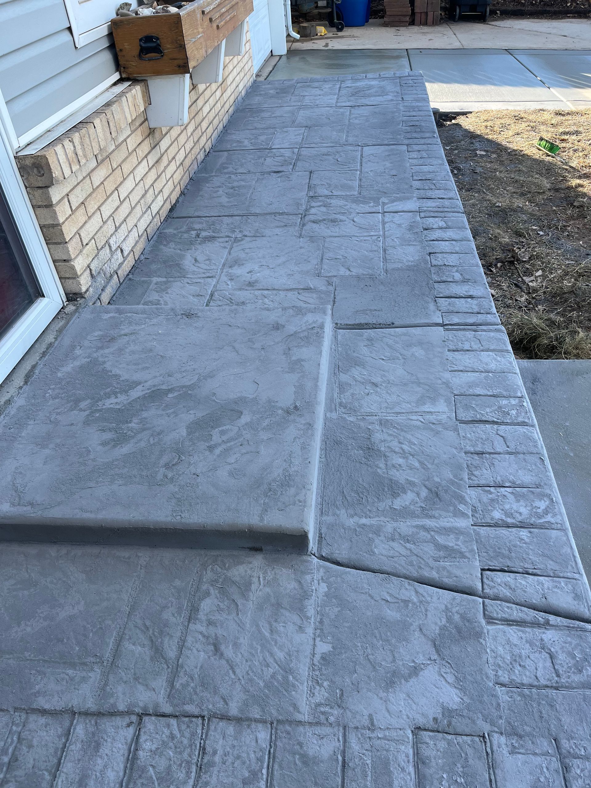 A concrete walkway leading to a house with a brick wall.