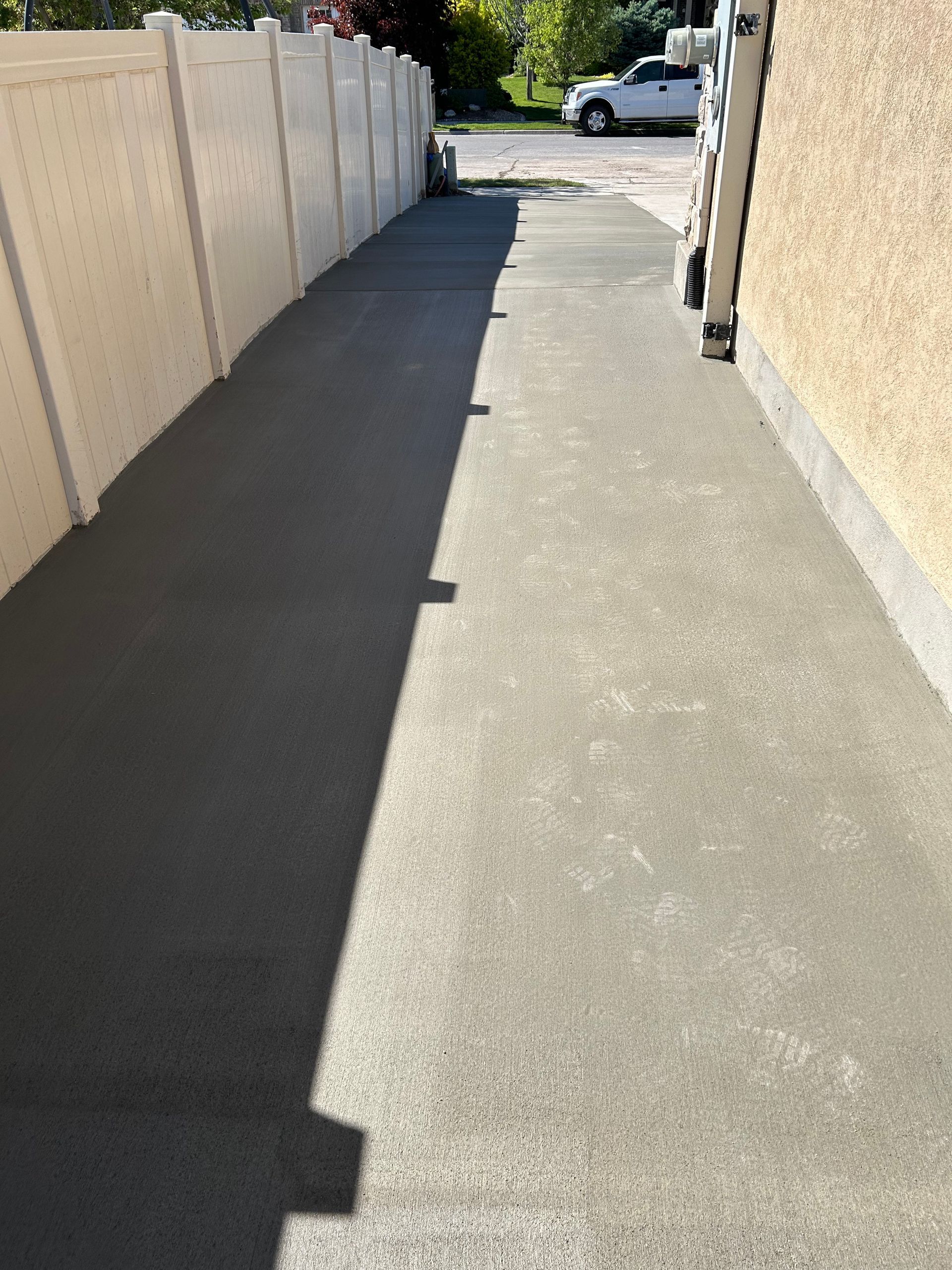 A sidewalk with a white fence and a white truck parked in the background.