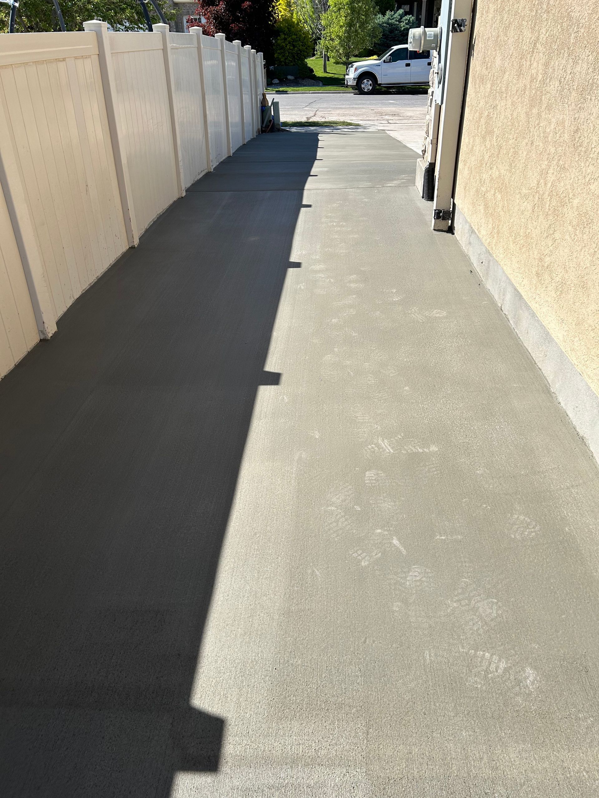 A concrete walkway leading to a house with a white fence.