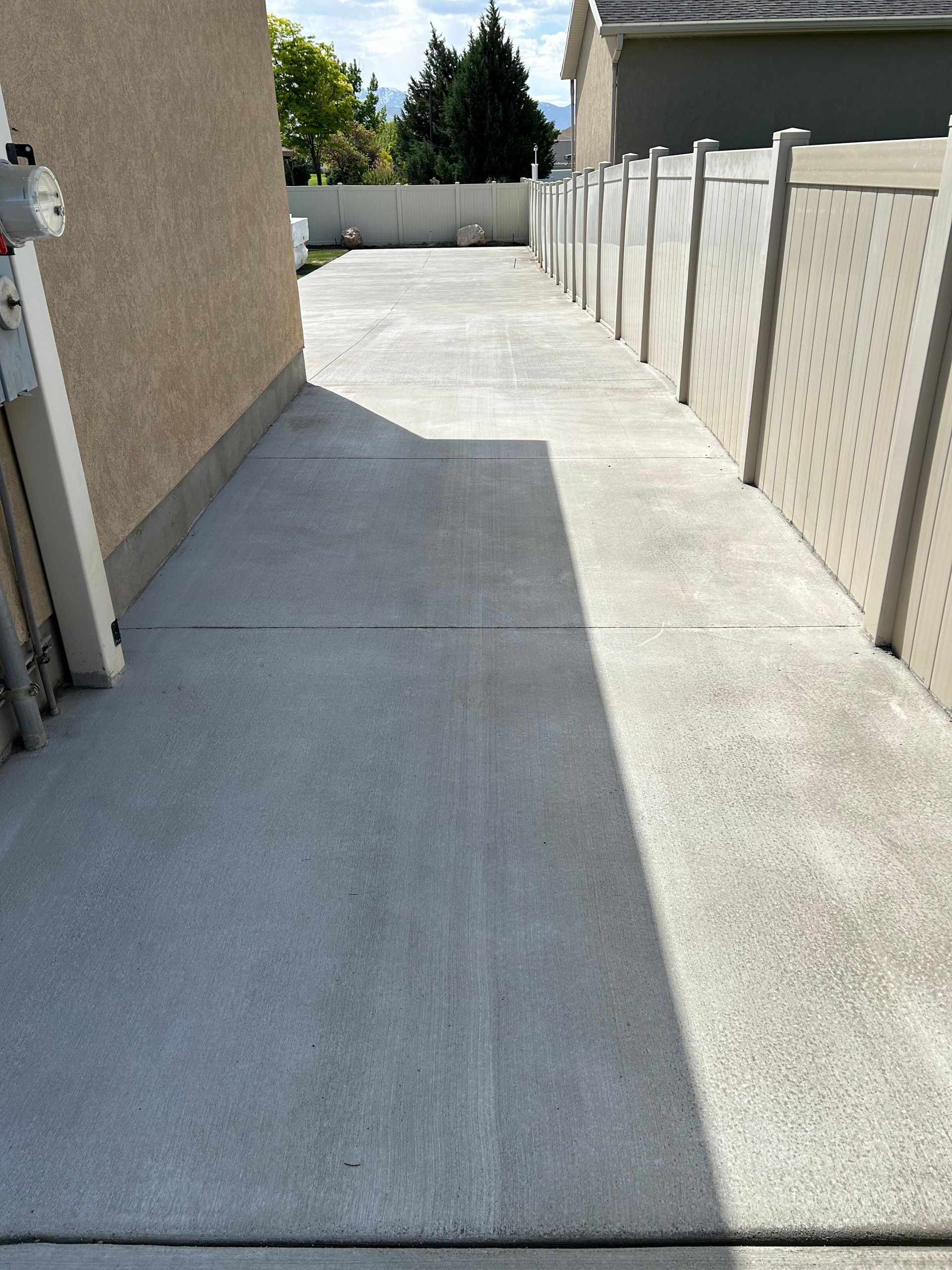 A concrete driveway leading to a house with a white fence.