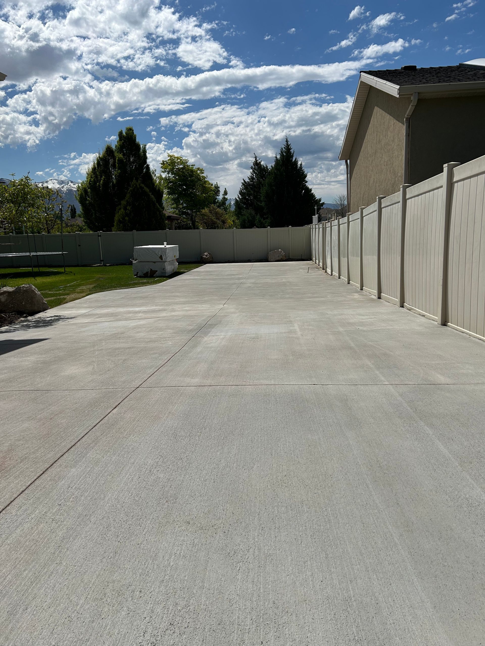 A concrete driveway with a white fence and a house in the background