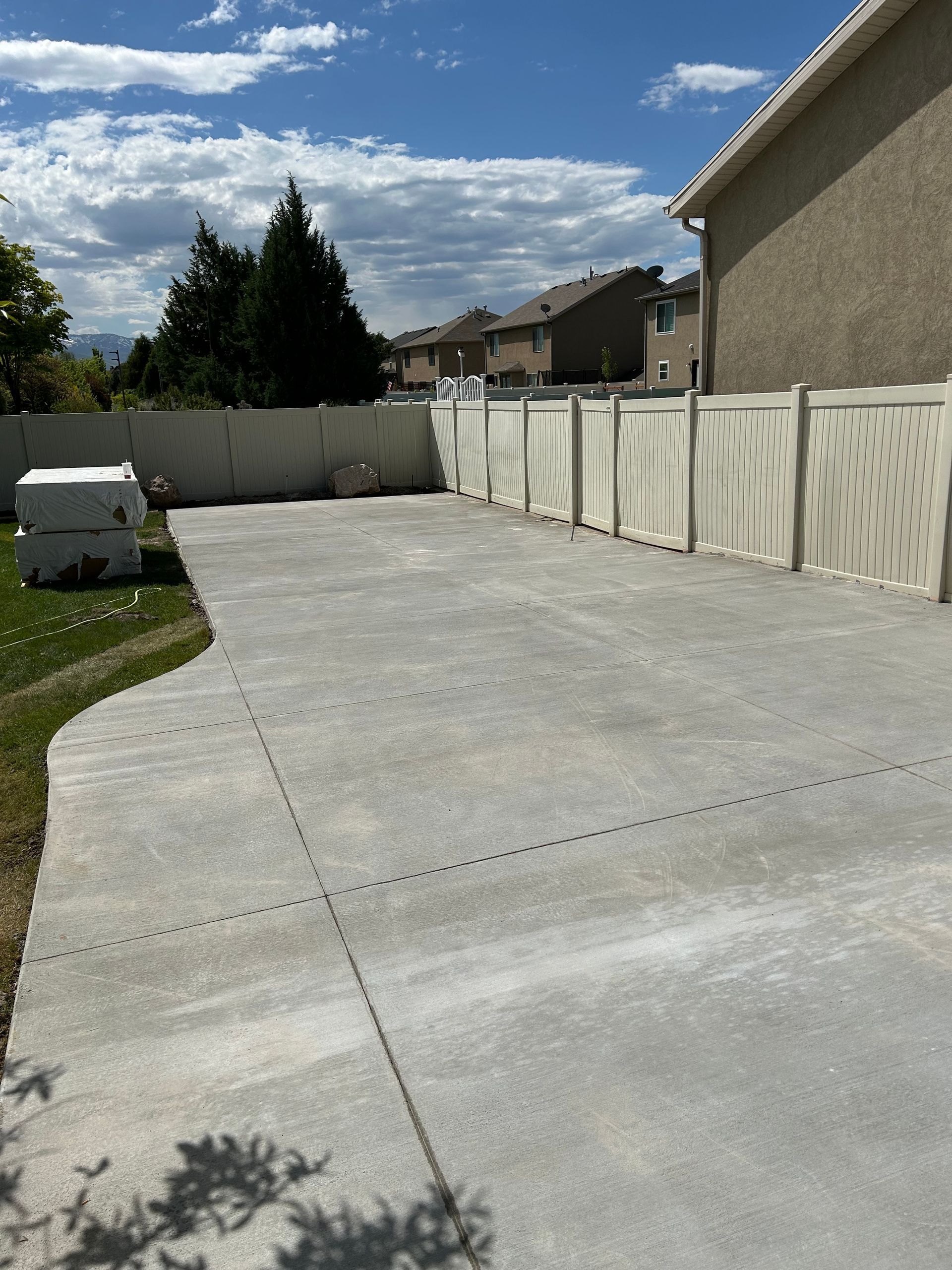 A concrete driveway leading to a house with a white fence