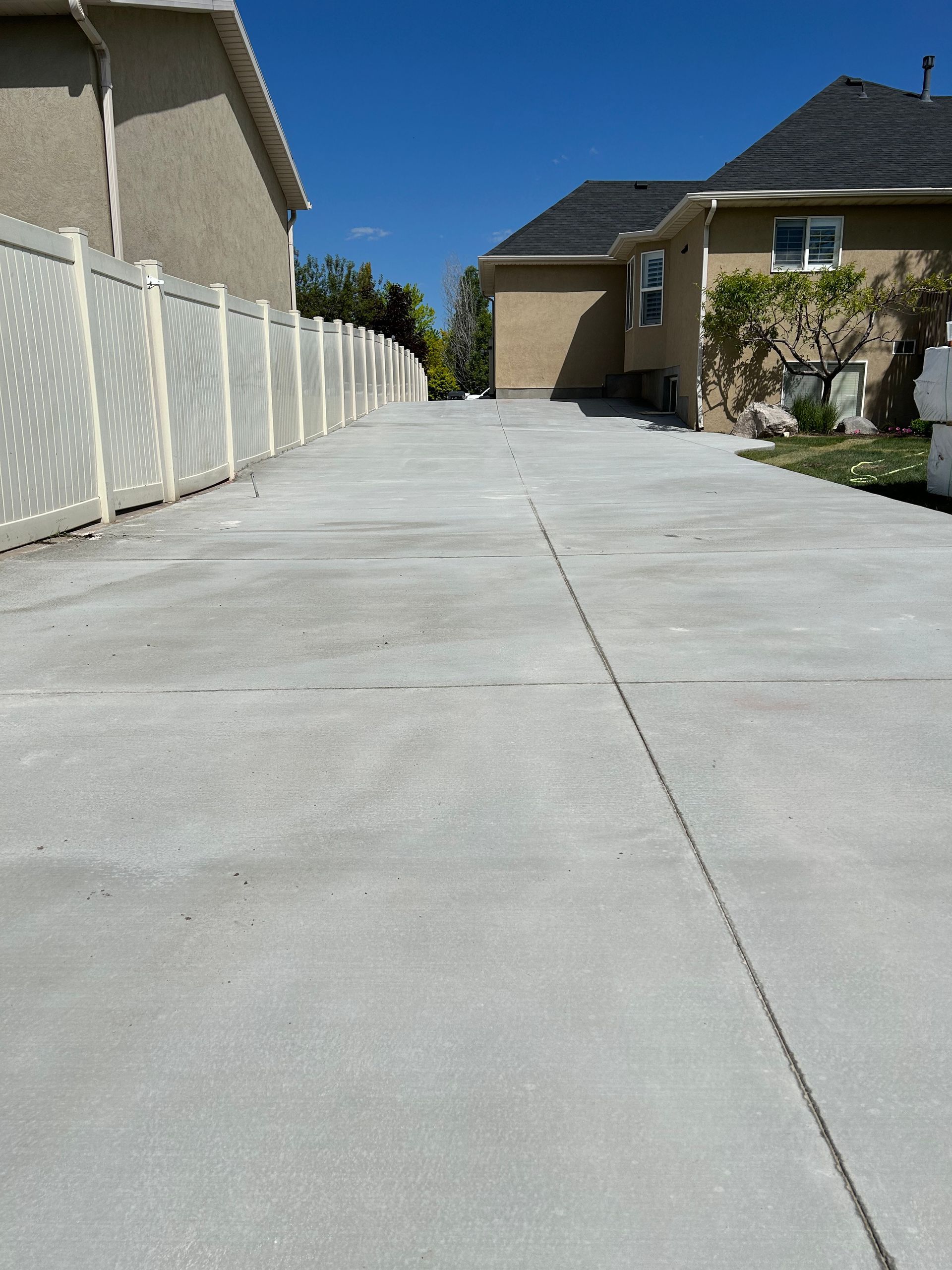 A concrete driveway leading to a house with a white fence