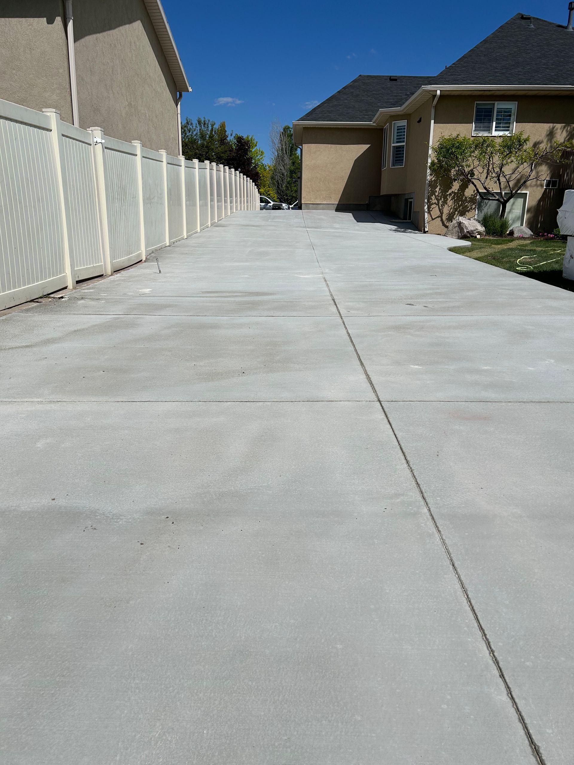 A concrete driveway leading to a house with a white fence