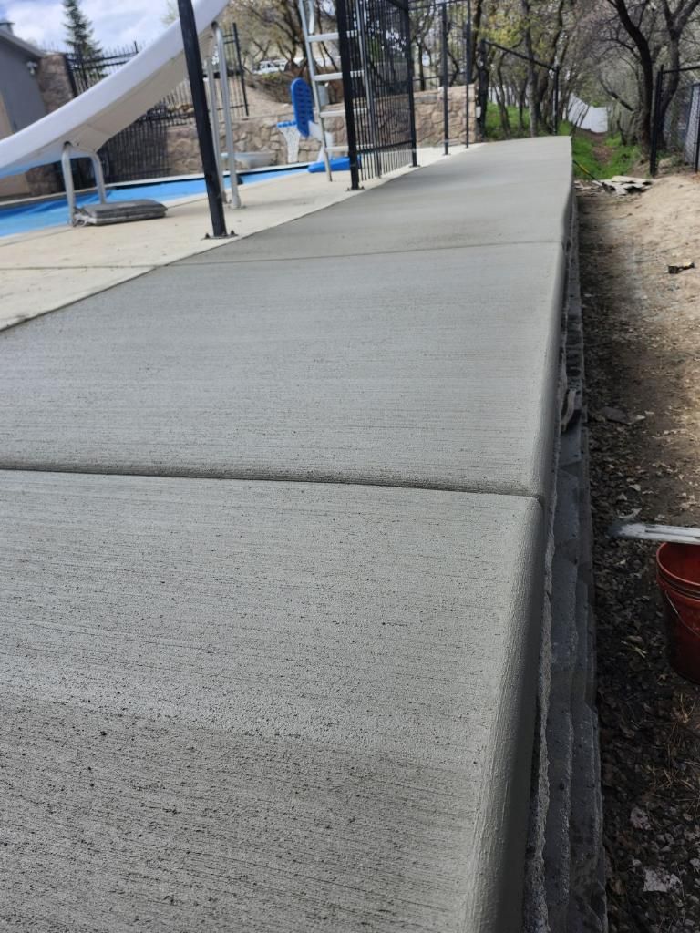 A concrete walkway leading to a pool with a slide in the background.