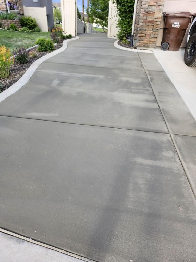A concrete driveway leading to a house with a trash can in the background.