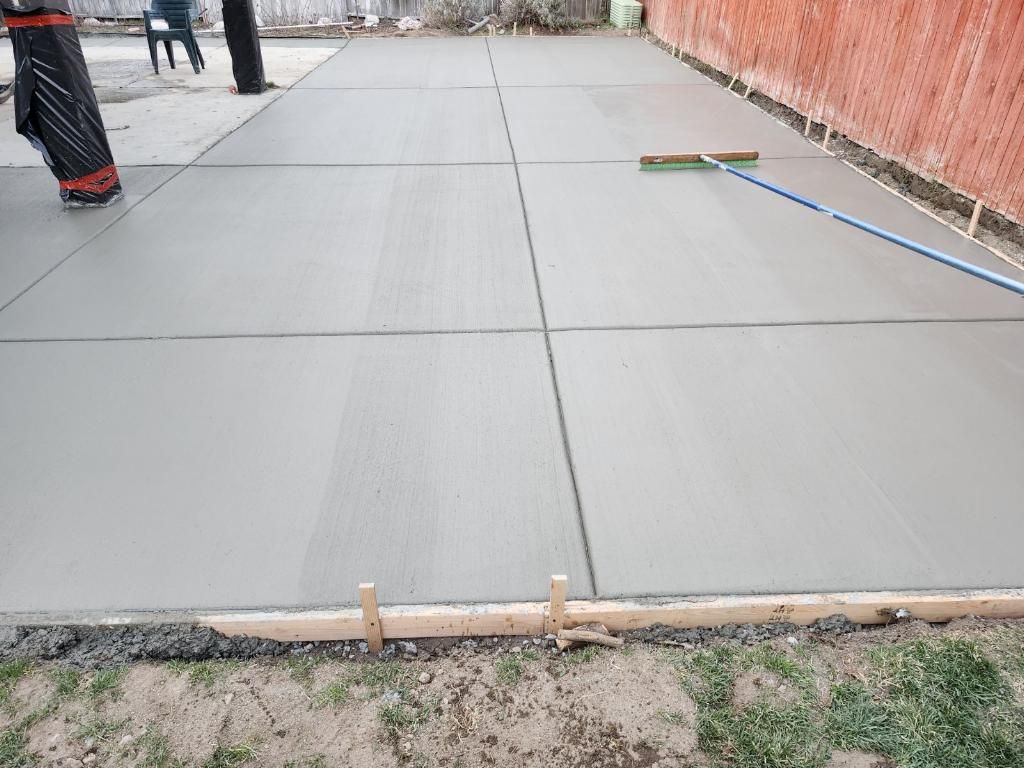 A person is spreading concrete on a patio with a broom.