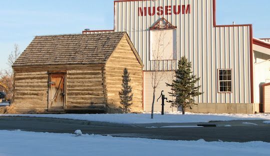 A museum building with a log cabin in front of it.