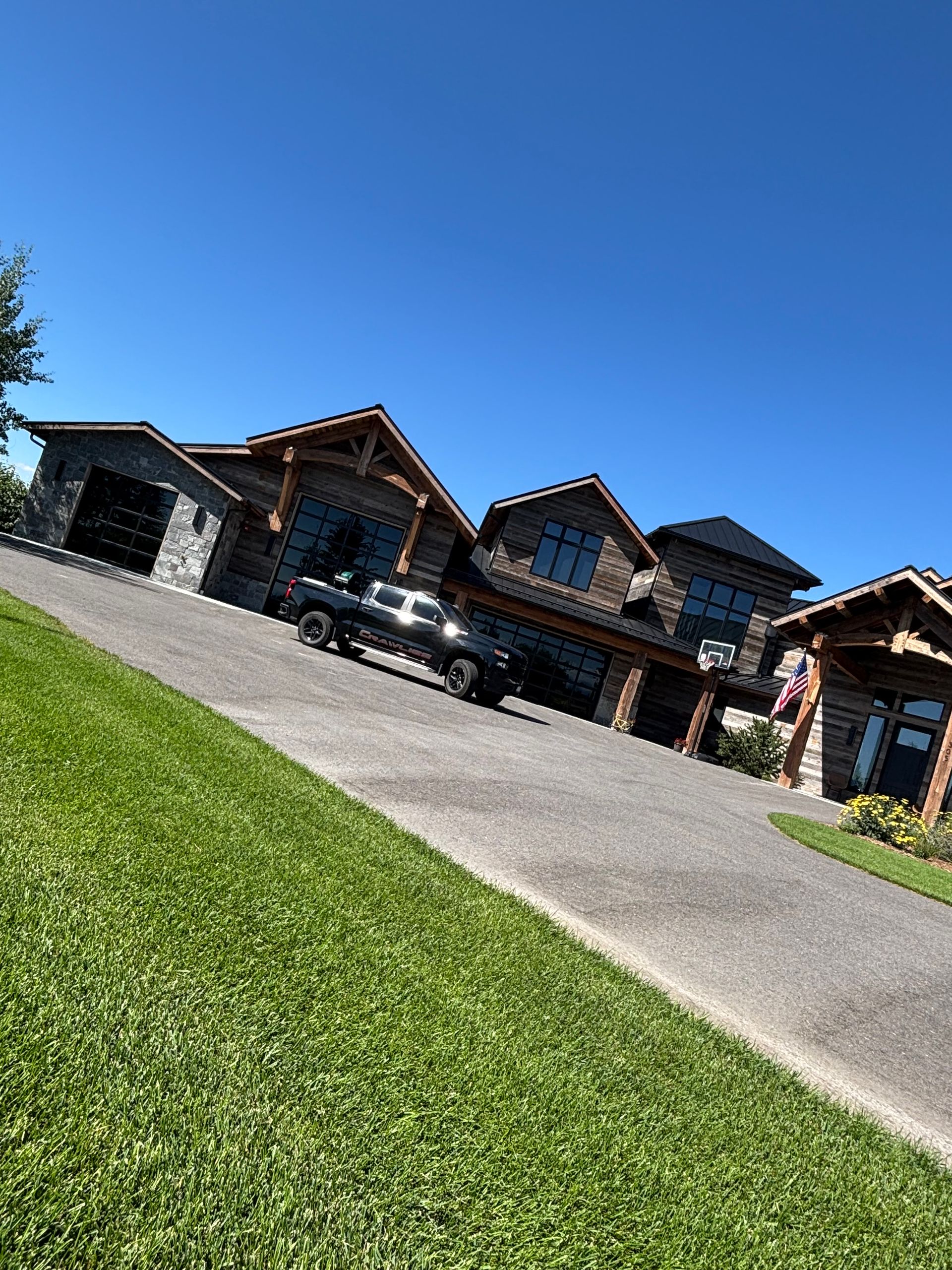 Large log house with a black pickup truck on the driveway, bright blue sky, and green grass.