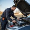 Mechanic, outdoors, working on car engine with tools. Blue uniform, inspecting parts.