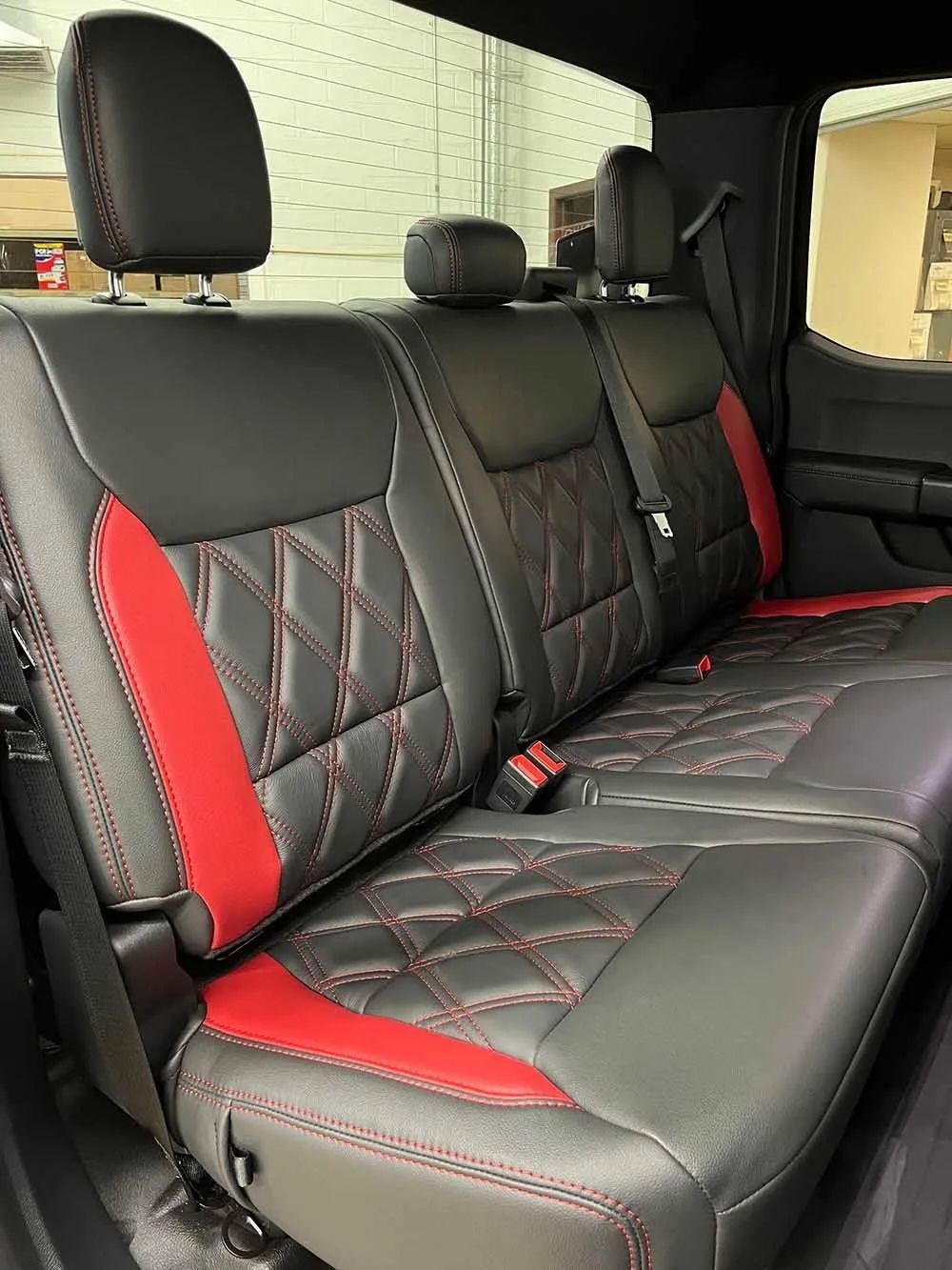 The back seat of a truck with black and red seat covers