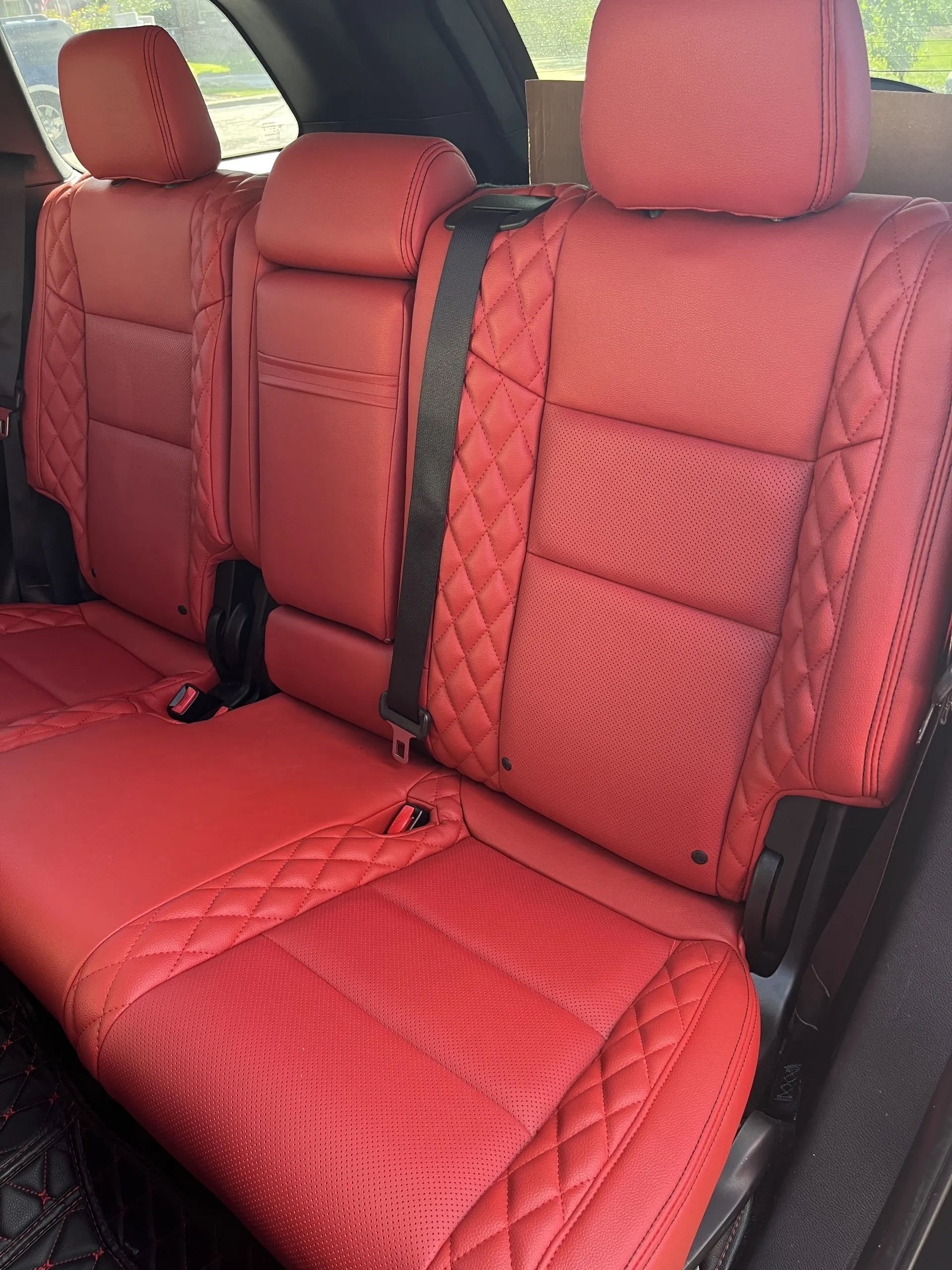 The back seat of a car with red seats and a black seat belt