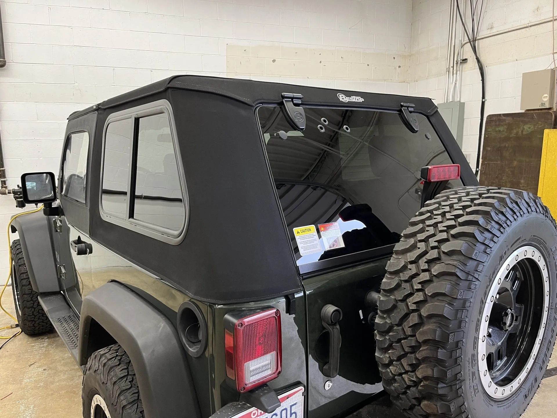 A black jeep with a hard top is parked in a garage