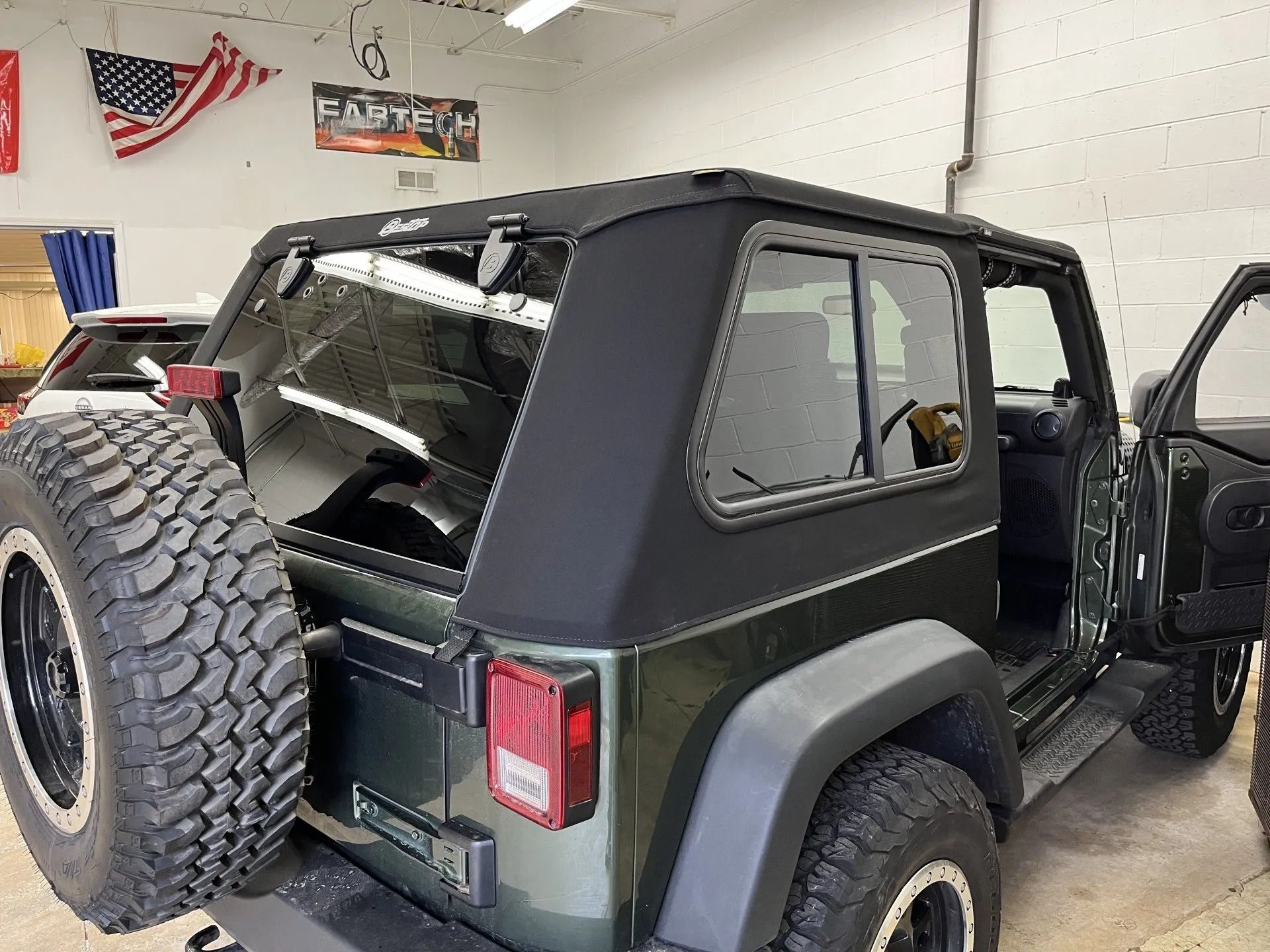 A black jeep is parked in a garage with its doors open