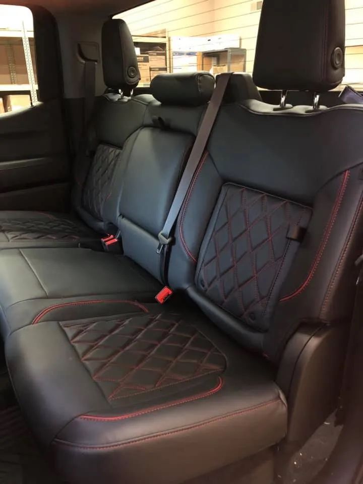 The back seat of a truck with black leather seat covers and red stitching