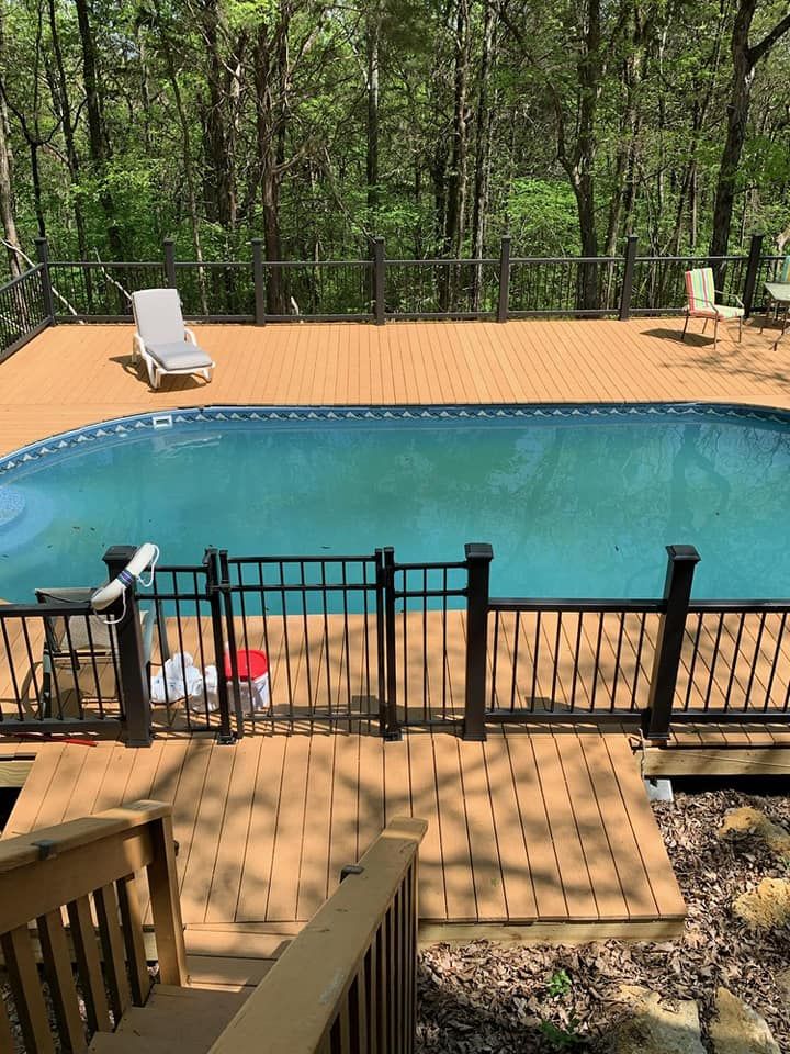 Backyard swimming pool with tan deck, black fence, and lounge chairs amid trees