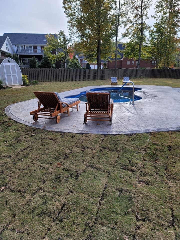 Backyard patio with two wooden chairs around a small pool, bordered by grass and a fence.