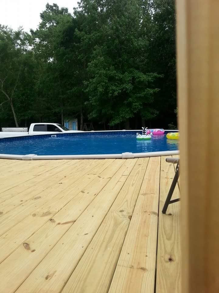 Backyard pool with blue water beside a wooden deck and trees in the background
