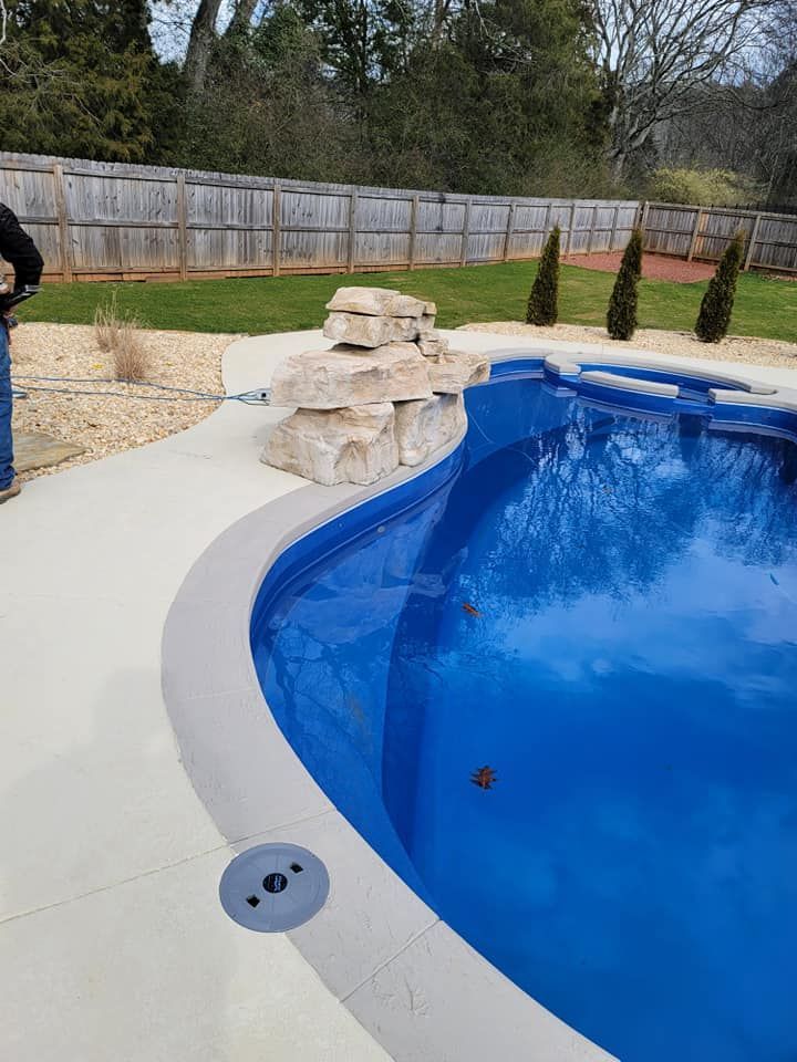 Backyard pool with curved blue water, light concrete deck, and stacked stone waterfall feature