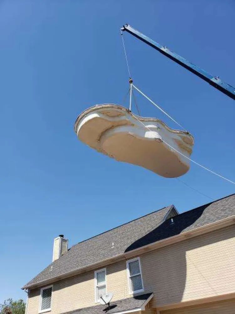 Crane lifting a large white sofa over a house roof against a blue sky