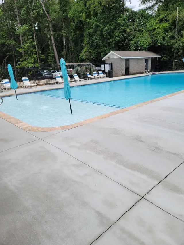 Outdoor swimming pool with blue umbrellas, lounge chairs, and a small cabana surrounded by trees