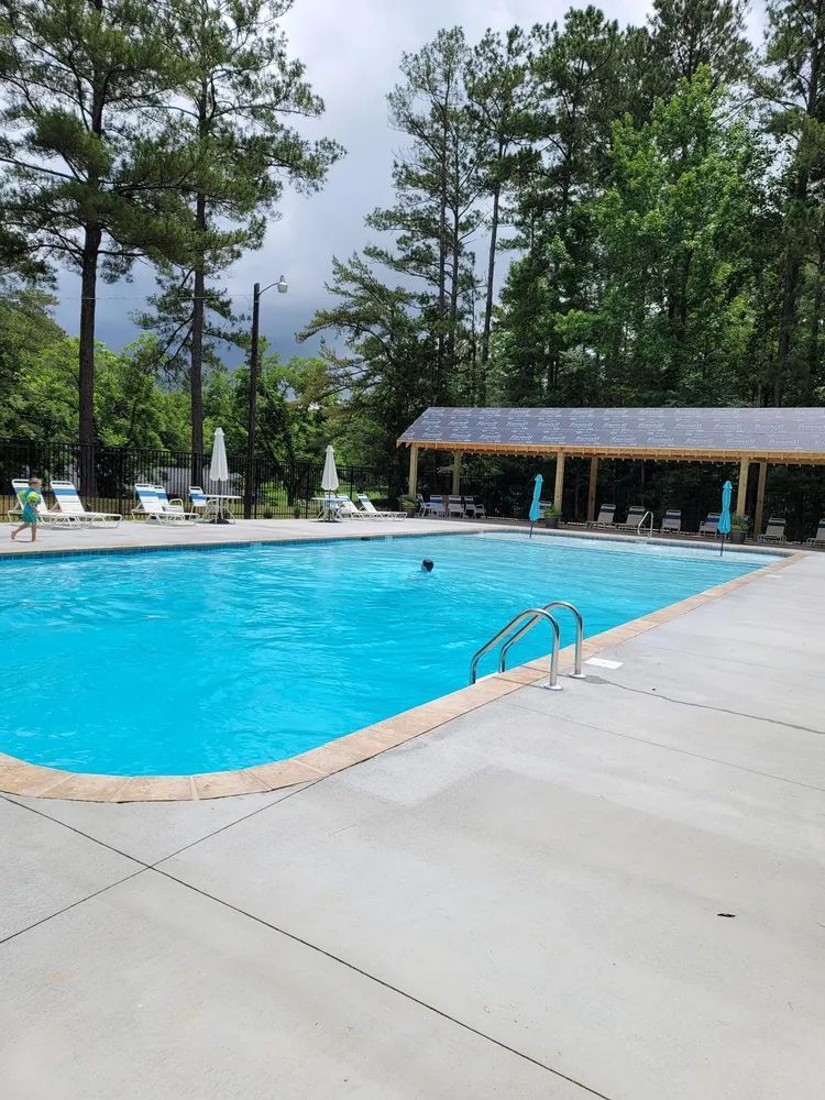 Outdoor swimming pool with lounge chairs, canopy, and pine trees under a cloudy sky