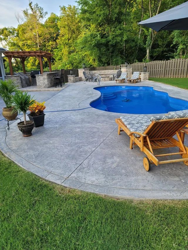 Backyard patio with a blue pool, lounge chair, potted plants, and pergola seating area