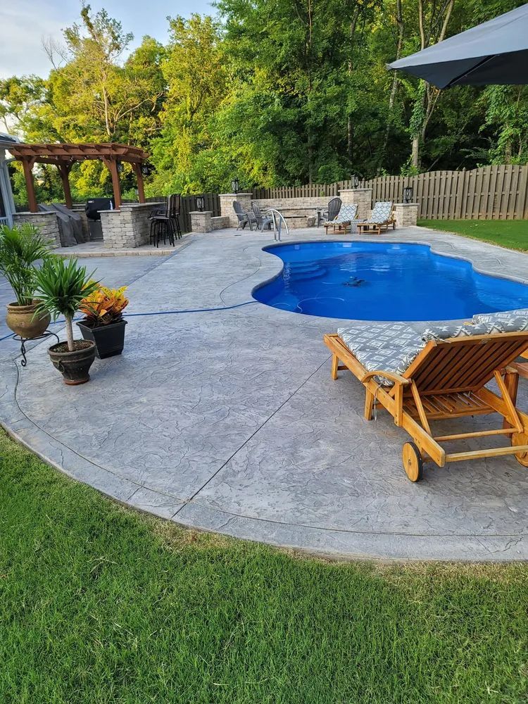 Backyard pool with stone patio, lounge chair, potted plants, and gazebo surrounded by trees