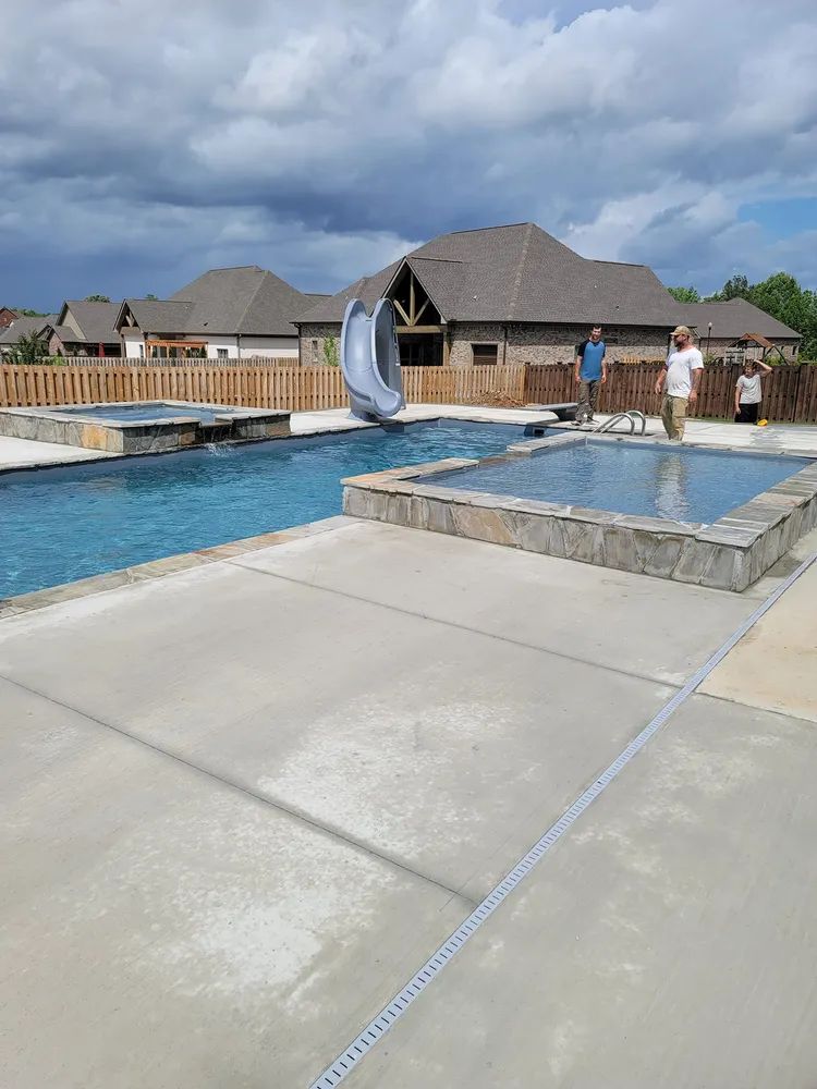 Outdoor resort pool with lounge chairs, a water feature, and cloudy sky overhead