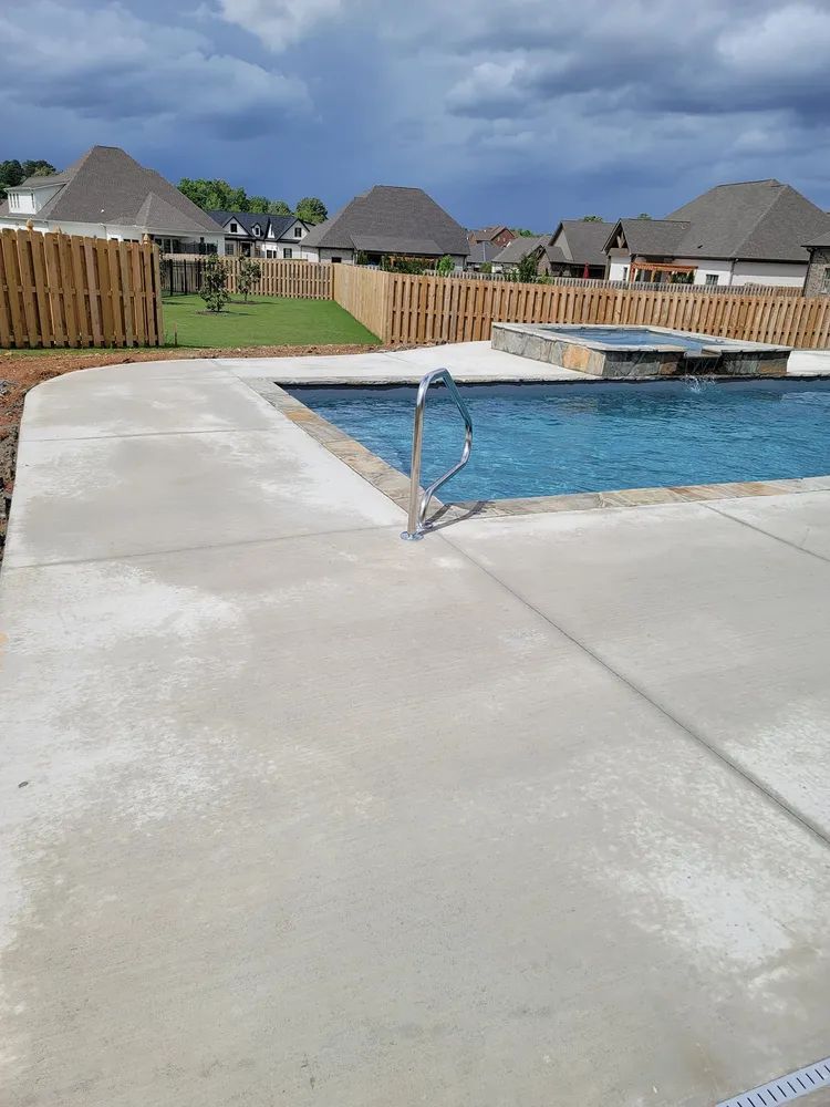 Backyard swimming pool with a concrete deck, fence, and houses in the background