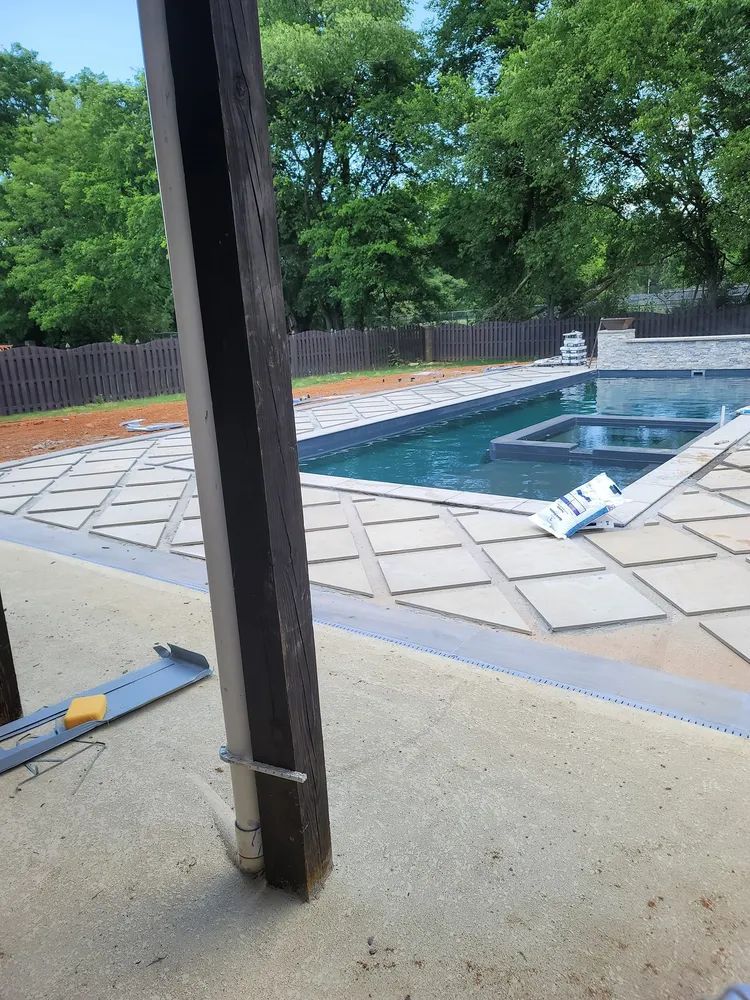 Backyard patio with covered pool, tan pavers, and a dark support post in the foreground