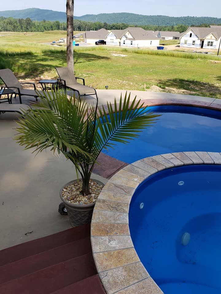 Patio with a potted palm beside a blue hot tub, overlooking a grassy yard and distant mountains