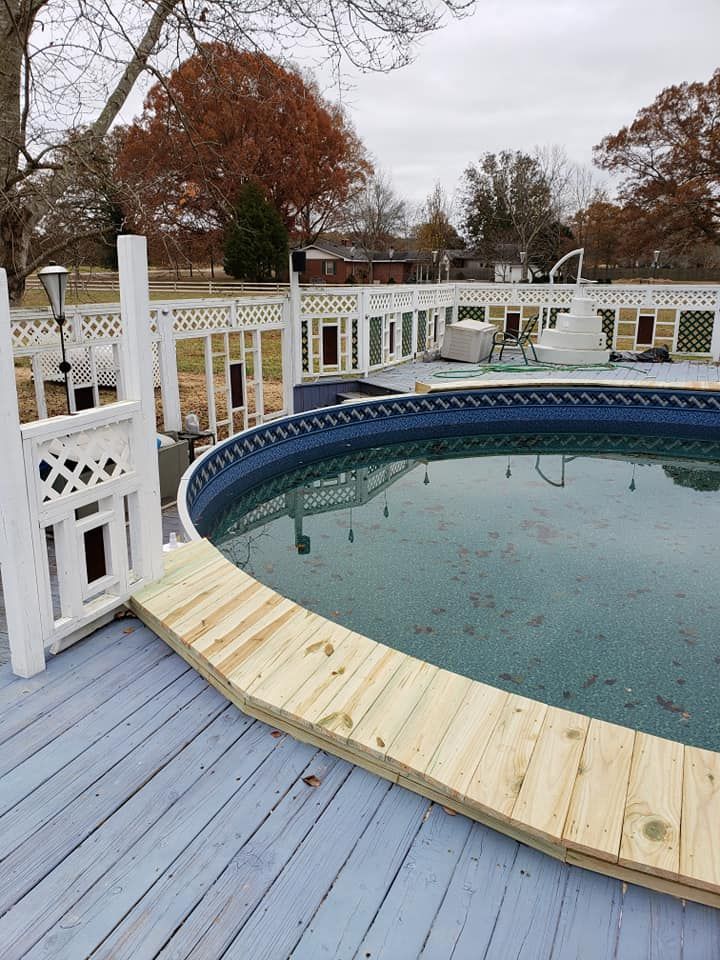Backyard above-ground pool with a blue deck and white fence on a cloudy day