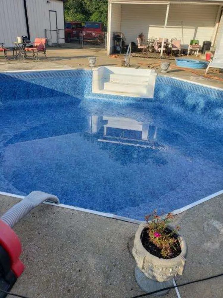 Blue swimming pool with a white bench in the water and patio furniture around it