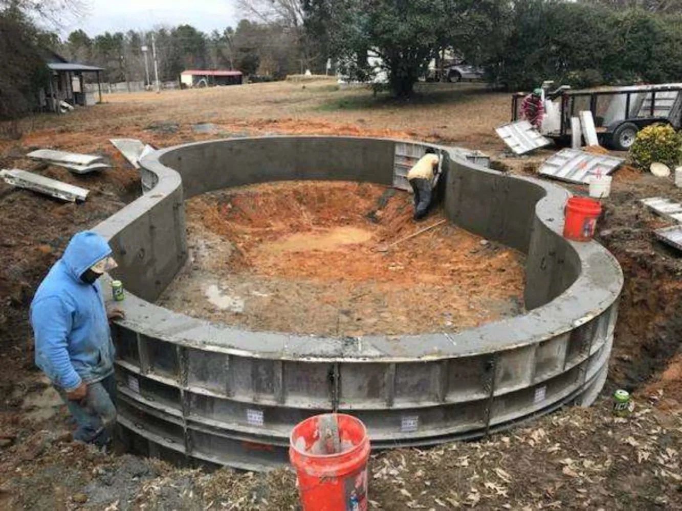 Workers building a large circular concrete tank in a muddy outdoor construction site