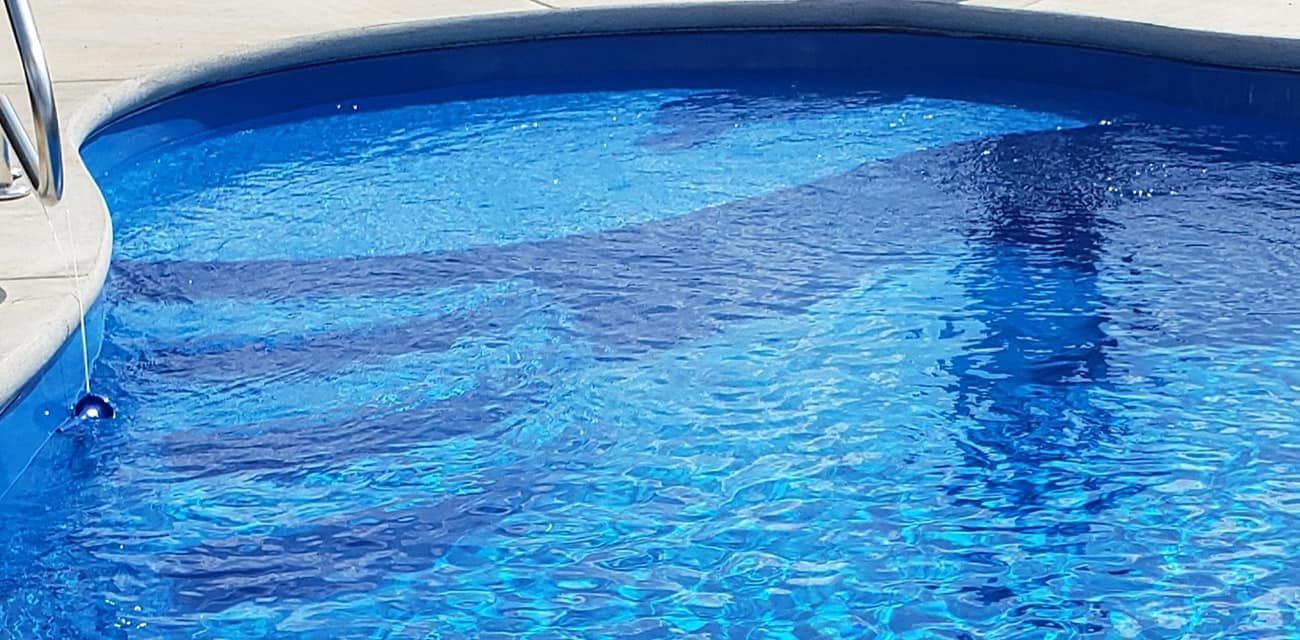 Blue swimming pool water with a white poolside edge and a dark reflection on the surface